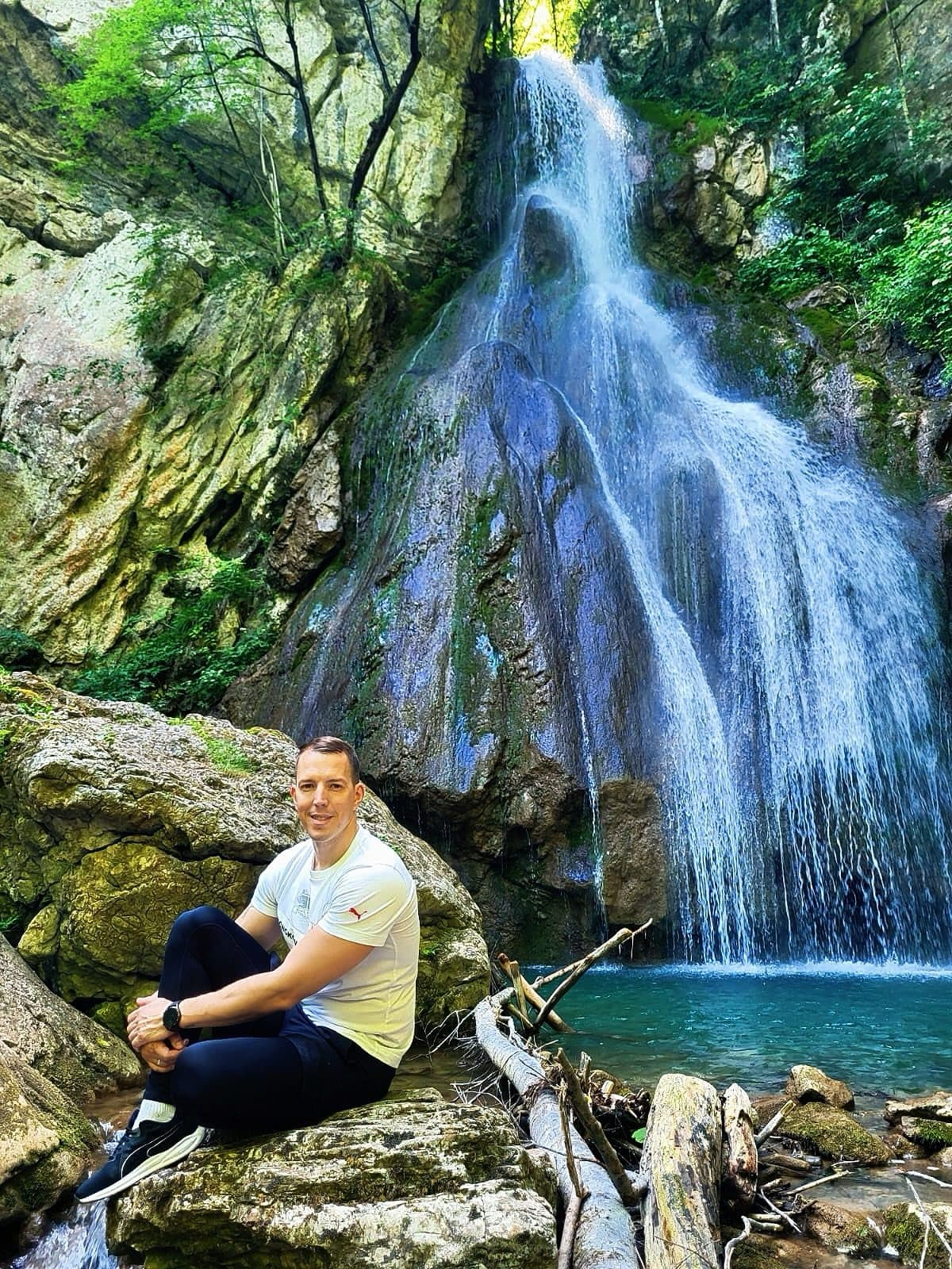 A man sitting on a rock in front of a waterfall in a green forest