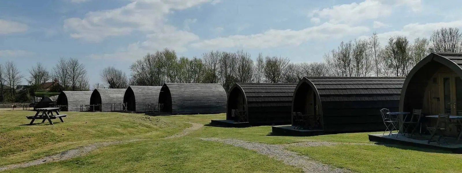 A row of modern wooden glamping cabins on a green lawn