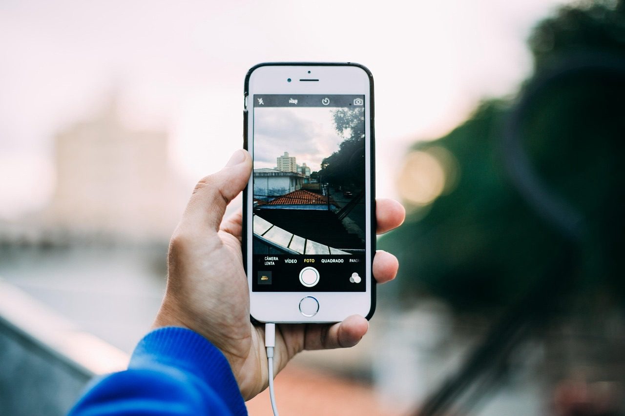 A hand holding a smartphone photographing a city skyline at golden hour