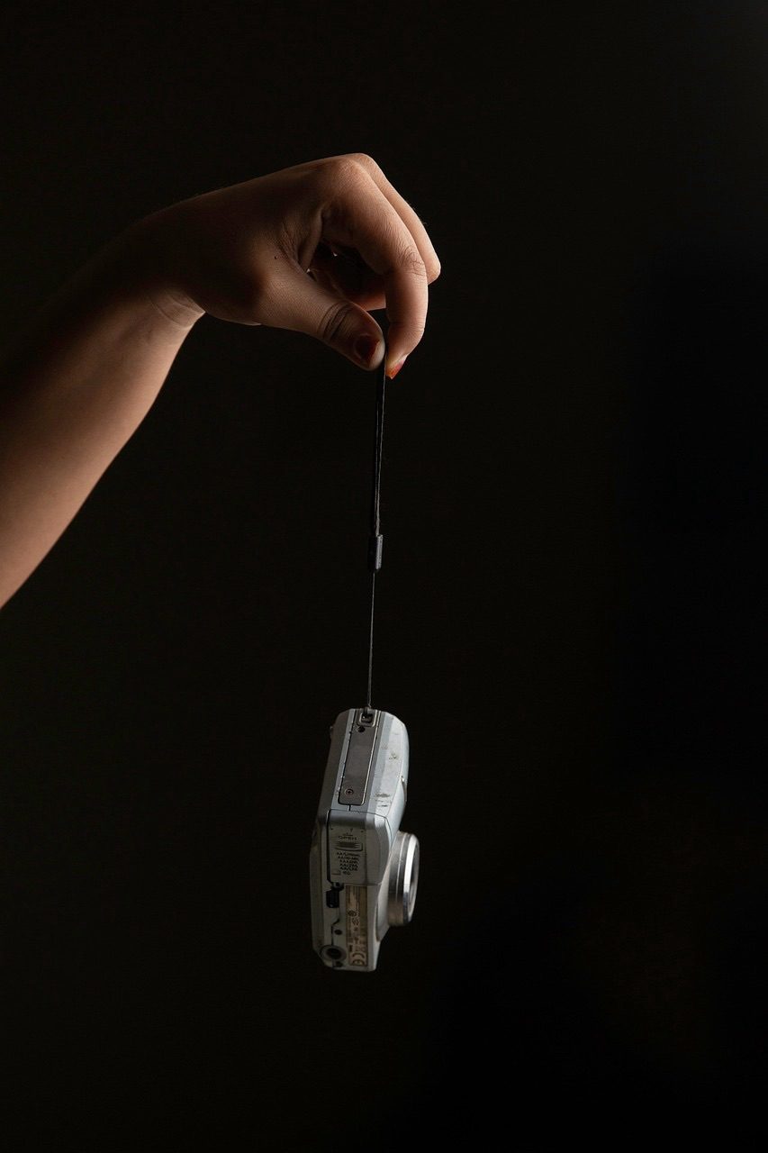 A hand dangling a vintage silver digital camera by its strap, a symbol of the weight of memory